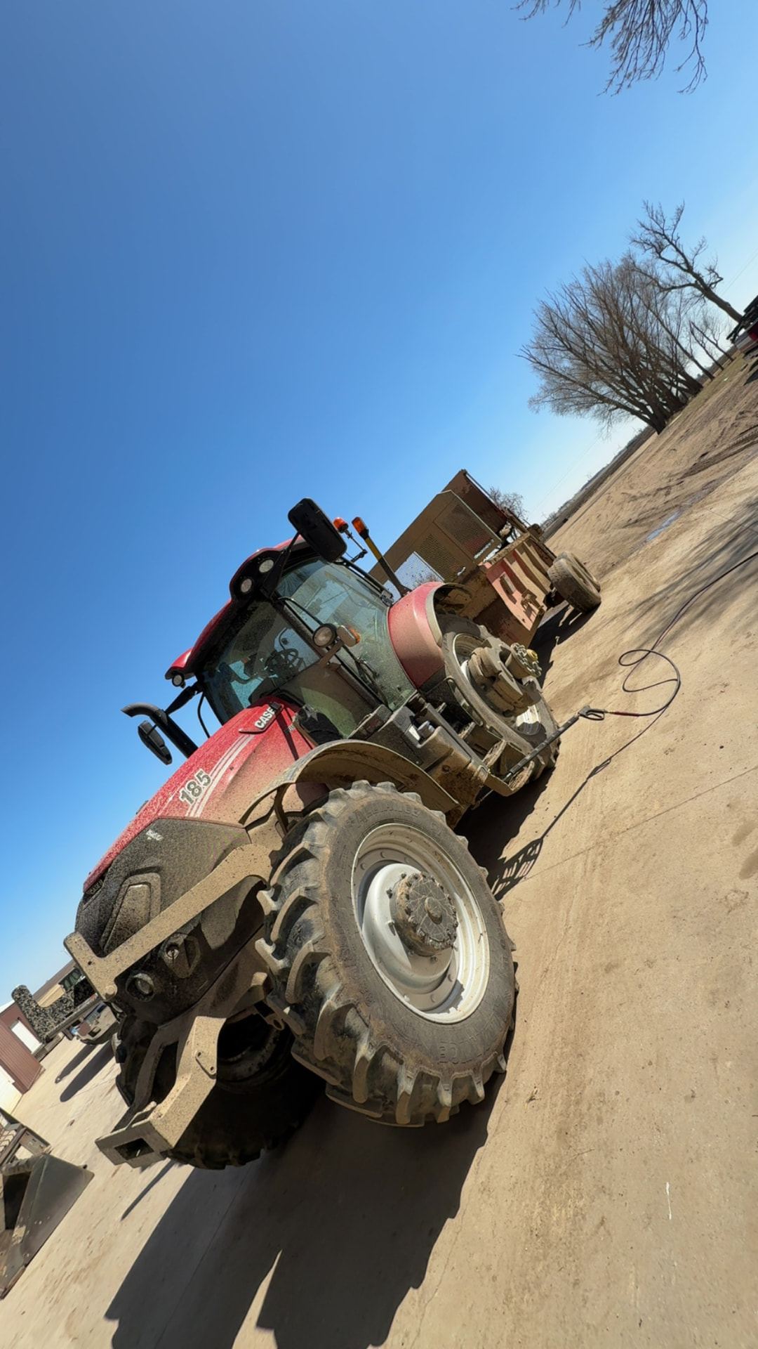 Muddy Case IH 185 tractor hooked to a spreader